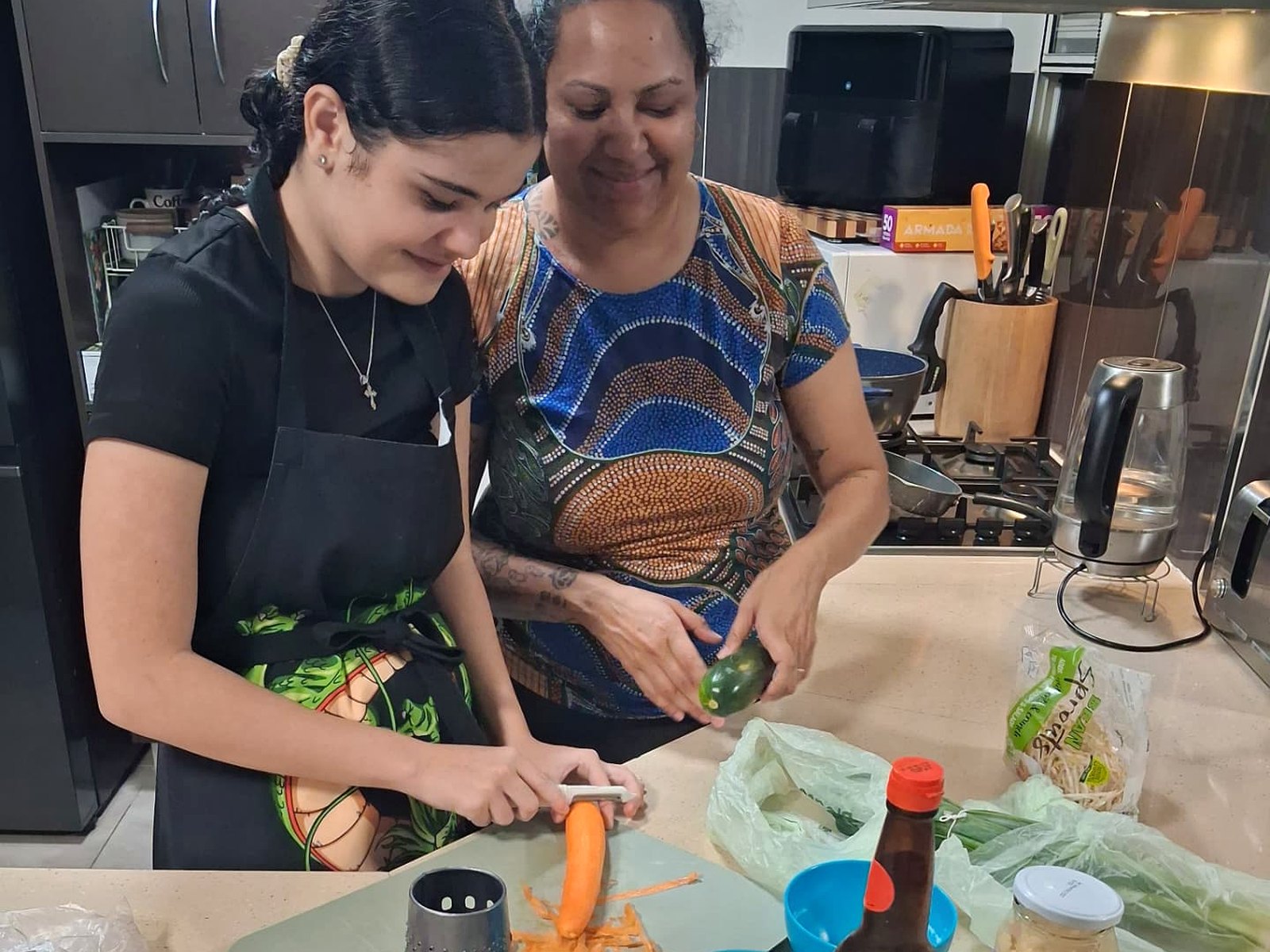 A young person and adult preparing vegetables together in a home kitchen.